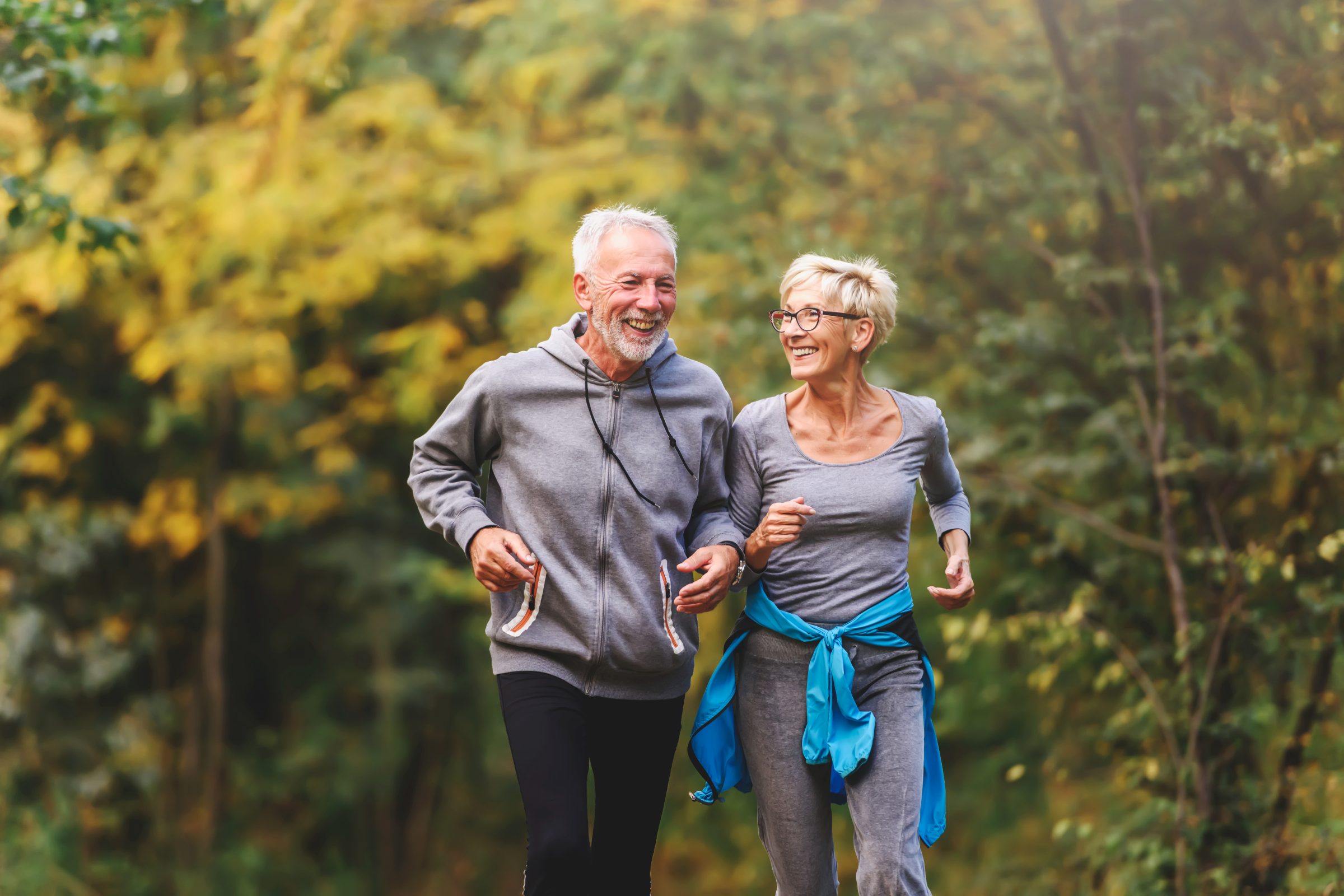 An older couple jogging together on a forest trail