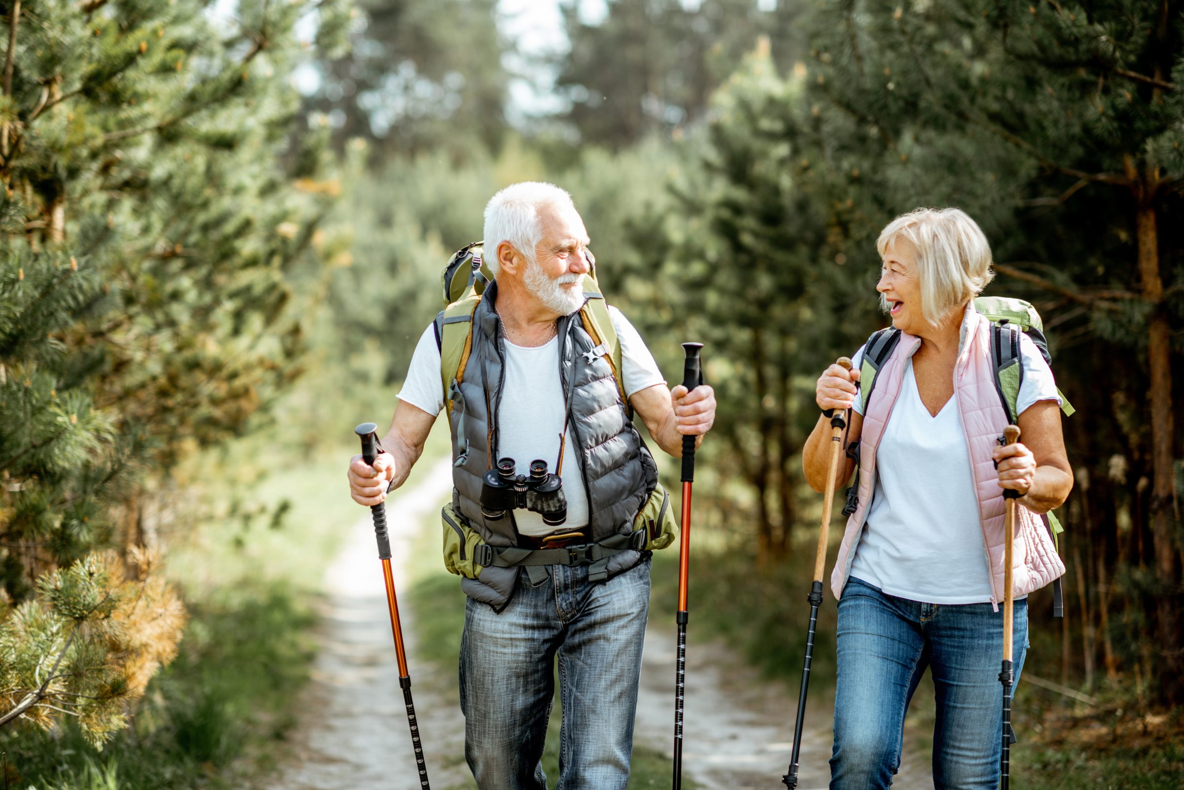 An older couple hiking with trekking poles on a forest trail
