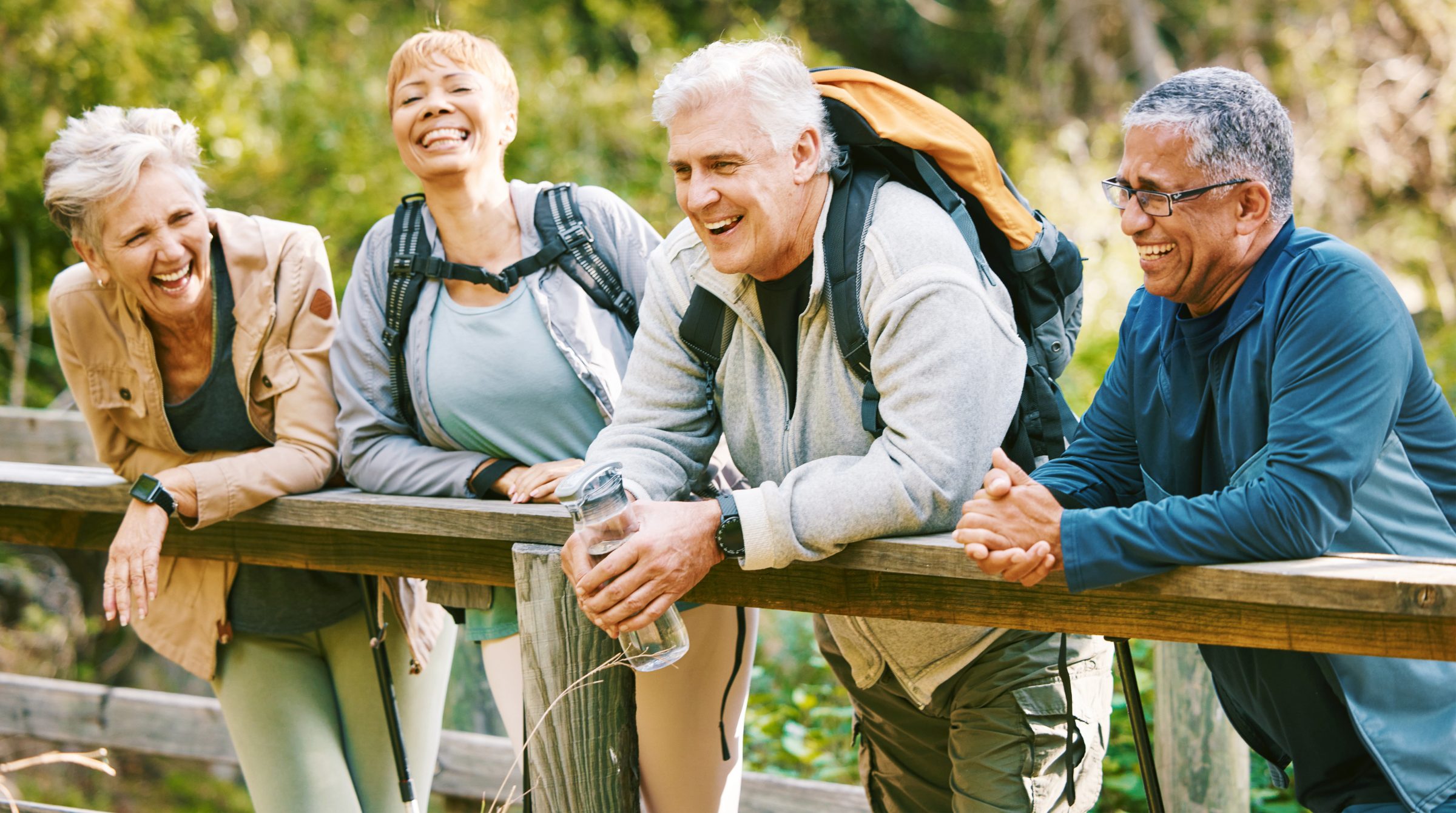 Four older friends with backpacks laughing at a trail railing
