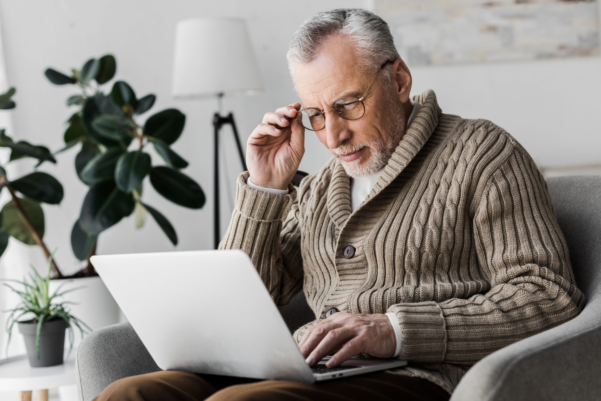 An older man adjusting his glasses while using a laptop