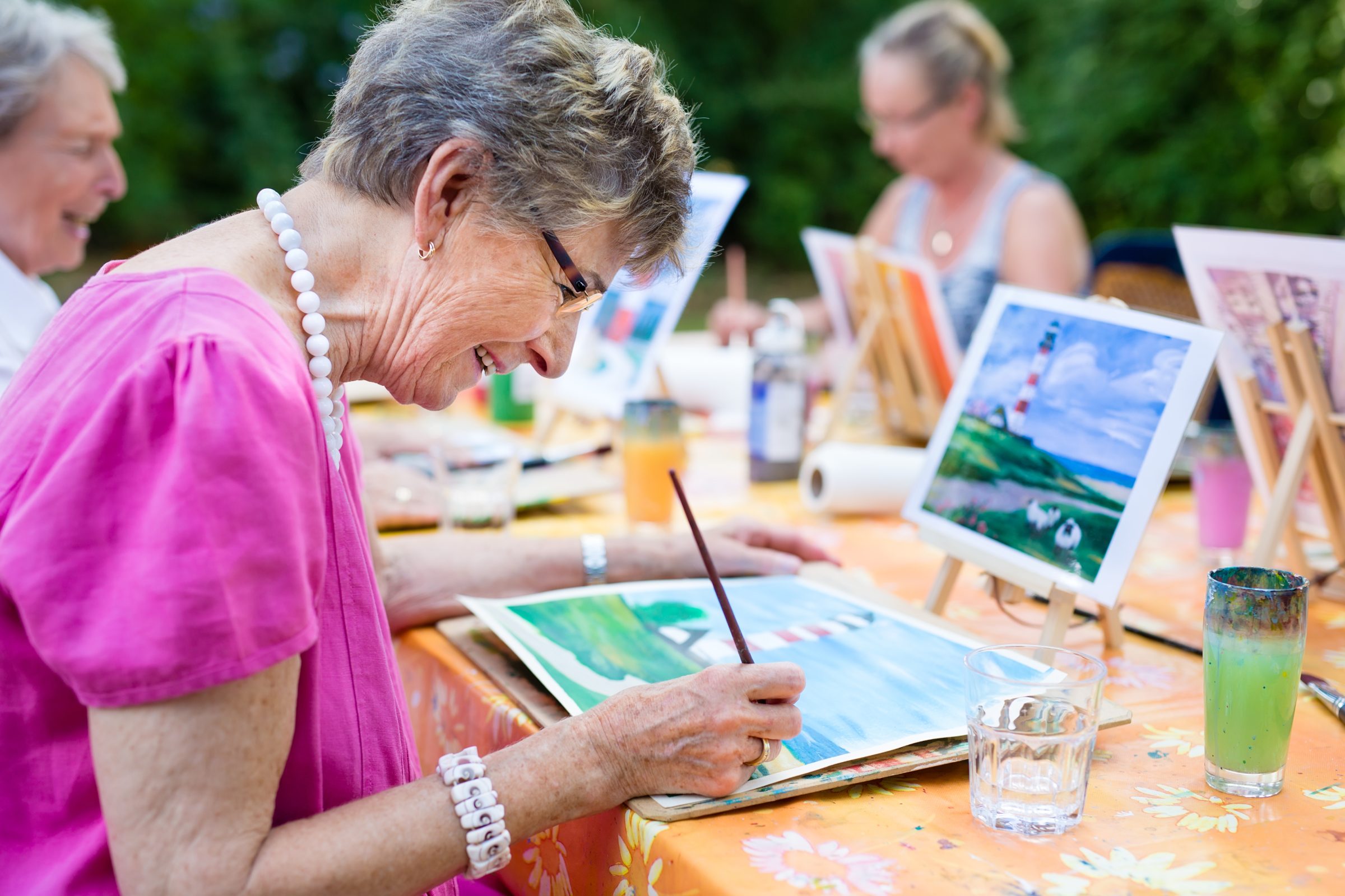 An older woman painting a landscape in an art class