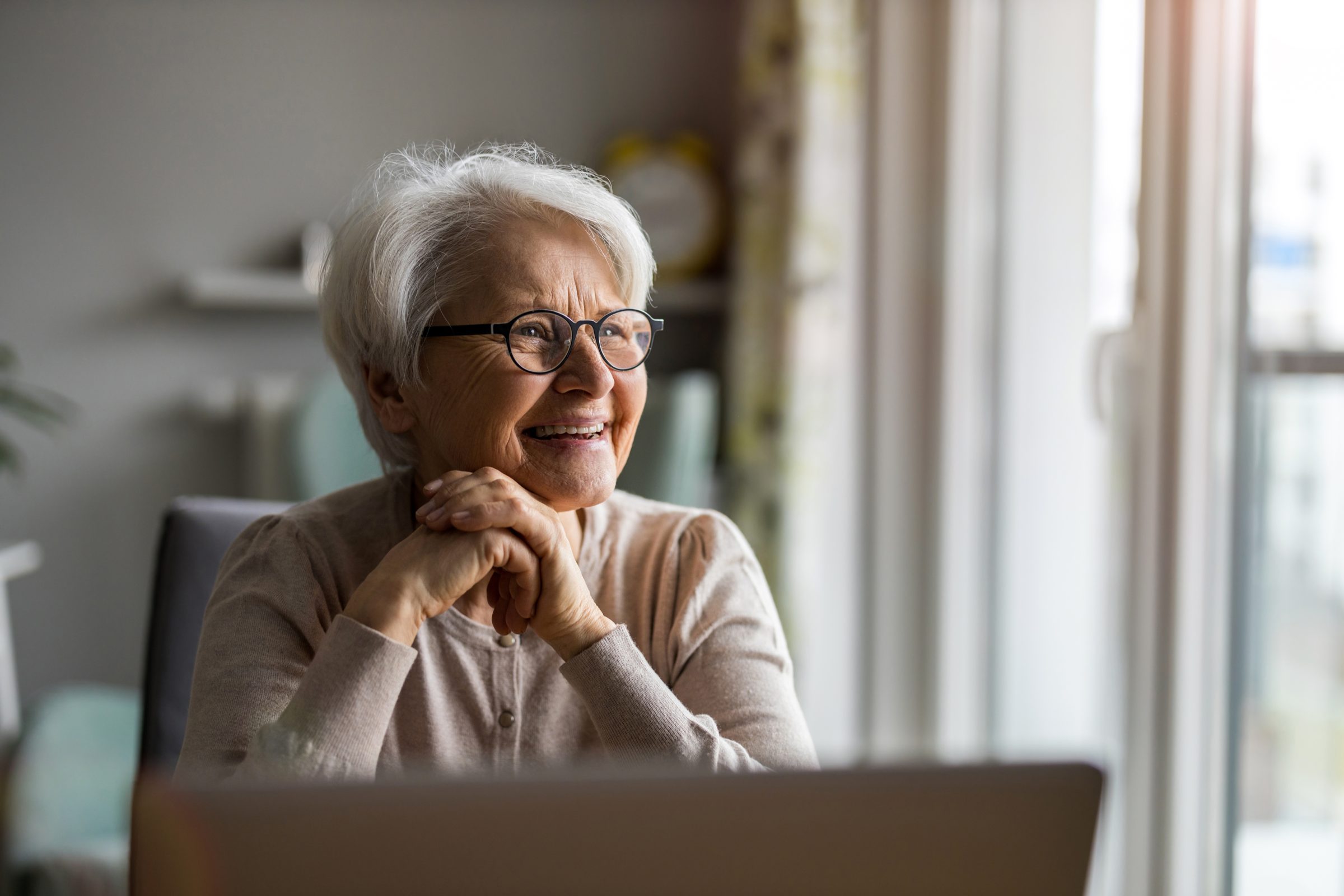 An older woman smiling at a table by a sunny window
